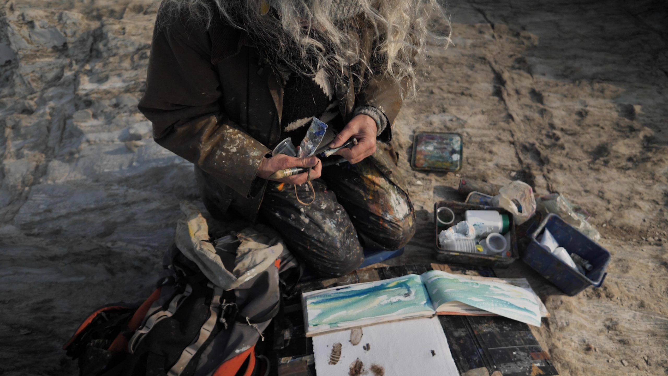 The rucksack, unpacked — A surface, two brushes, primary colours, white, and a binding medium.